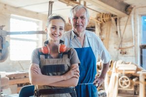 Senior master carpenter with his granddaughter in the wood workshop looking at camera