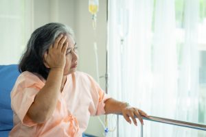 old woman sat on the sick bed used hand to hold her head , expressing concern about her illness as well as worrying about the cost of treatment , recover from her illness in the hospital long time