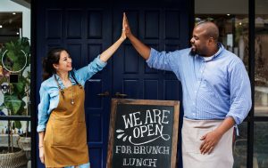 Cheerful business owners standing with open blackboard
