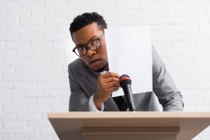 scared african american speaker hiding behind paper during business conference