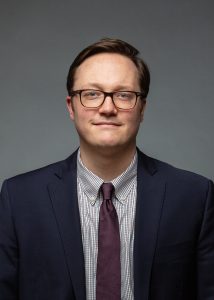 Professional Headshot of Stephen Wagner, Esq. Stephen is a white man with short brown hair. He is wearing glasses and a navy suit with a maroon tie.